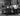 Black & White photo of four Men standing around a car on a city street.